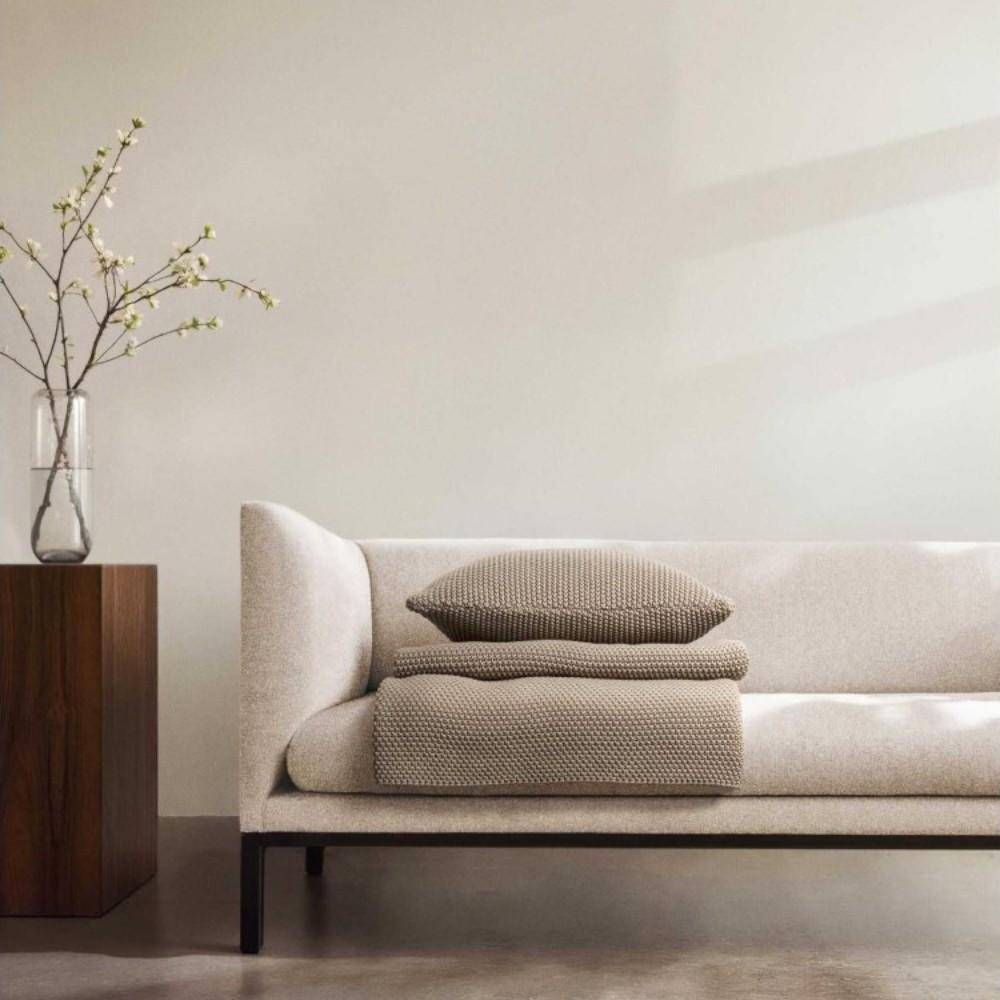 Strickplaid Nordic Knit in Oakwood auf modernem Sofa mit passendem Kissen in minimalistischem Wohnraum