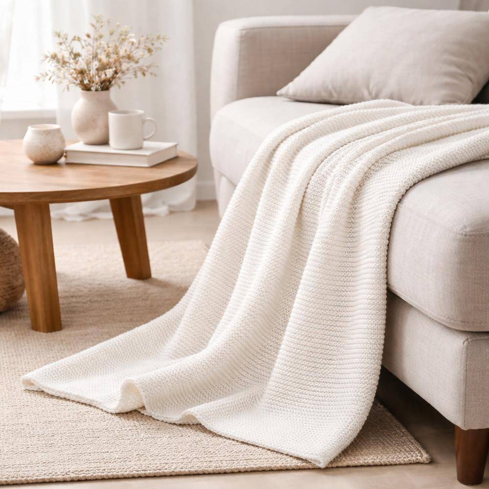 Off-White Strickplaid auf Sofa drapiert in hellem Wohnzimmer mit Holztisch und dekorativen Accessoires